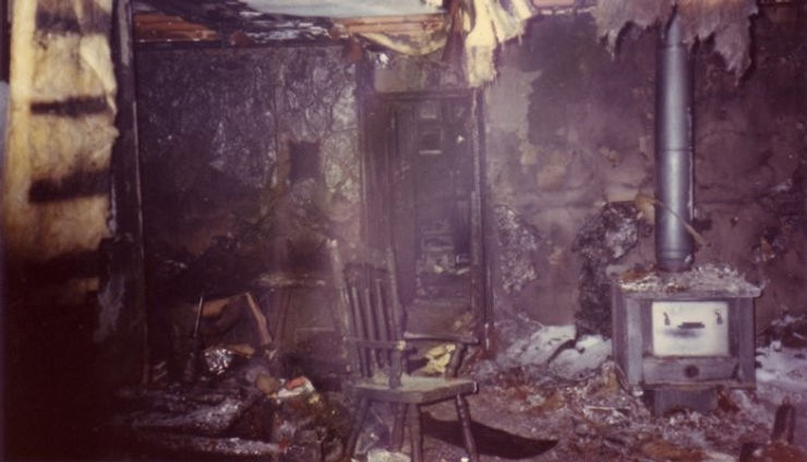 Photo of living room post house fire. Charred with insulation falling from ceiling.